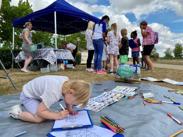 Young child colouring in a butterfly sheet with other children stood by a Butterfly Conservation stand in the background