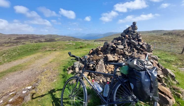 Simon Saville's bike laden with packs, leaned against a cairn overlooking Scottish scenery